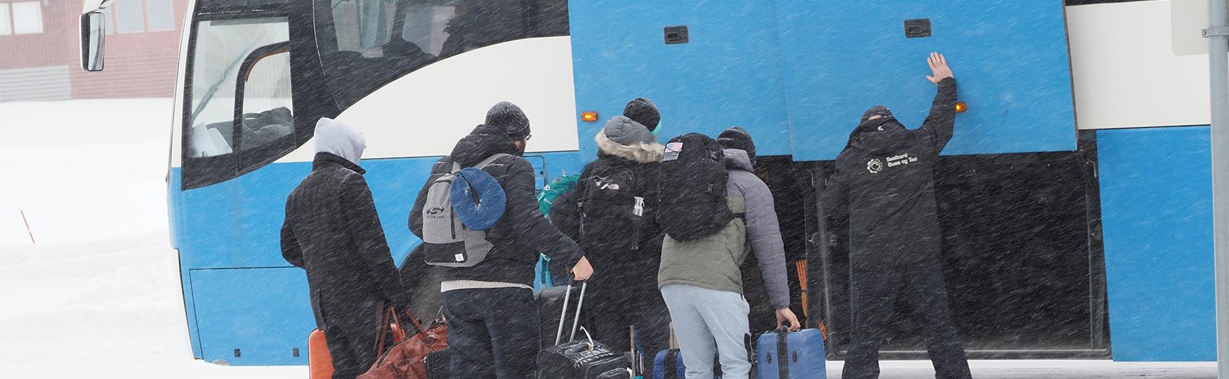 En bussjåfør som hjelper en gruppe gjester med å laste bagasje inn i en buss i tett snøvær
