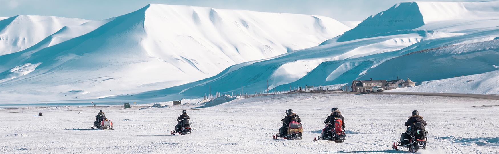 A guided group on snowmobiles driving through a snowy landscape
