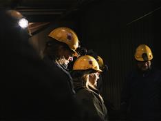 Personer i en mørk gruve som har på seg gule gruvehjelmer