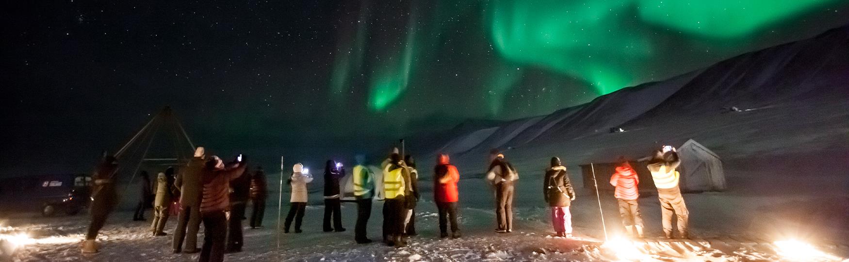 En gruppe med gjester som ser opp på nordlys på en mørk himmel