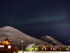Nordlys og fjell i bakgrunnen med opplyste fargerike hus i forgrunnen
