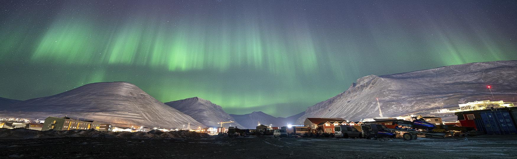 A town with snow-covered mountains and northern lights in the background