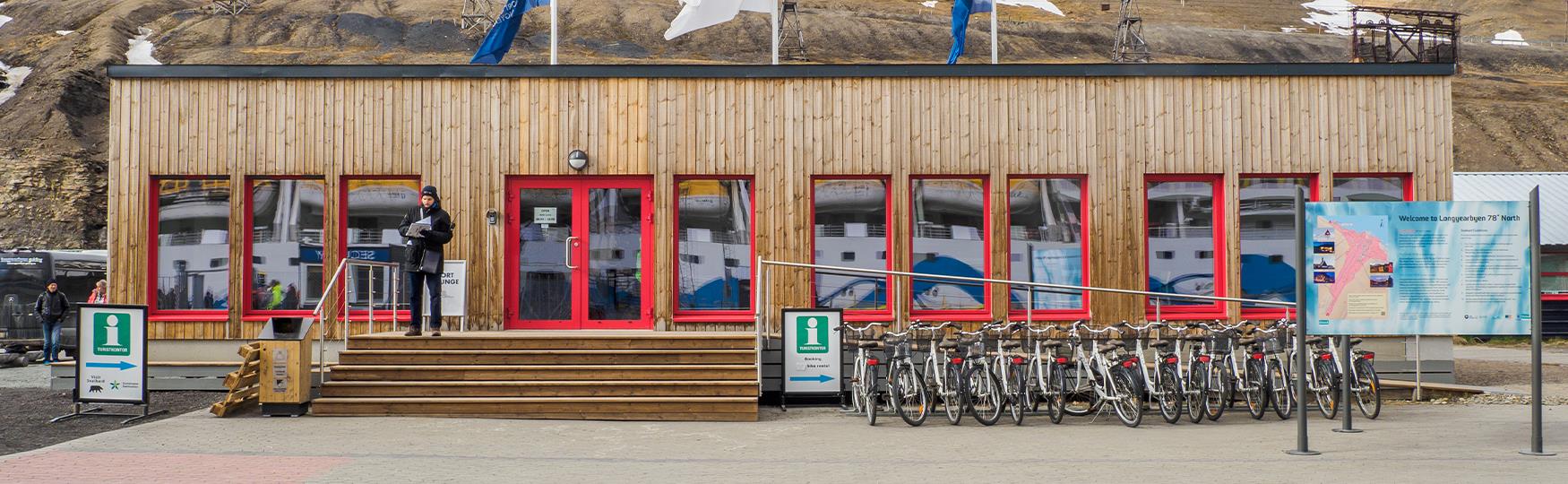 Open port lounge in the Port of Longyearbyen with a guest standing outside the front door, rental bikes and a map of Longyearbyen in the foreground