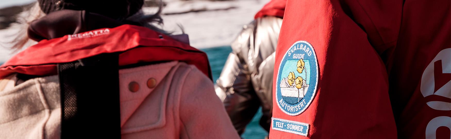 Gjester om bord en båt med en guide i forgrunnen som har et SGO-merke med autorisasjon som sommerguide på jakken sin.