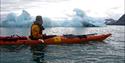 A guide in a kayak, in front of a small iceberg