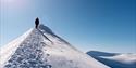 A hiker crossing the mountain ridge. Clear blue sky.