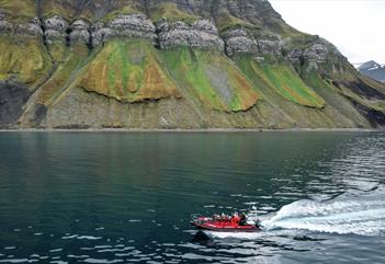 A RIB boat with guests and a guide sailing across a fjord with mountains in the background