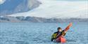 Two guests paddling in a double kayak on a fjord with a glacier behind them