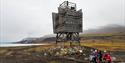 Gjester og en guide som tar en pause ved et gammelt kulturminne utenfor Barentsburg