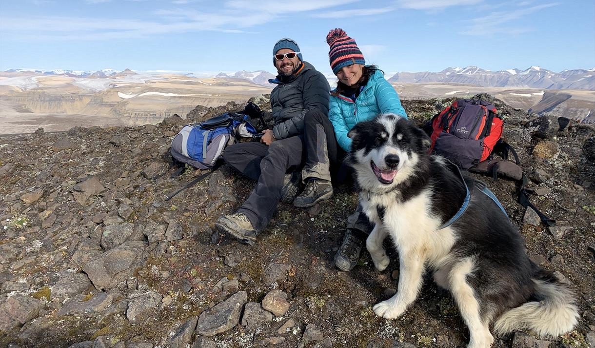 Two persons and a dog relaxing on top of a mountain