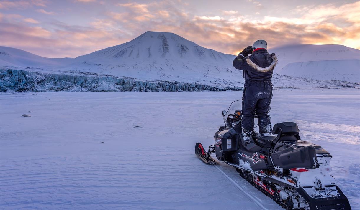 A guide standing on a snowmobile scouting out the terrain using binoculars