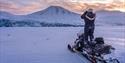 En guide som står på en snøscooter og speider i terrenget med en kikkert