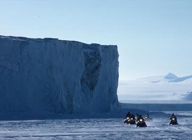 A tour group on snowmobiles with an ice wall in the background