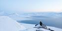 To personer som står på en fjelltopp og ser utover en fjord