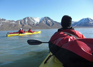 People kayaking on the sea in the foreground, with mountains in the background.
