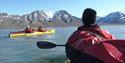 People kayaking on the sea in the foreground, with mountains in the background.