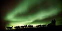 Northern lights and a silhouette of a sleddogteam pulling a sled with 2 people on it
