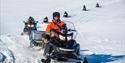 A guide leading a tour group on snowmobiles
