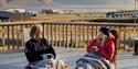 To gjester som sitter utendørs med pledd og drikker kaffe på en balkong