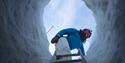 A person at the top of a ladder leading down into an ice cave