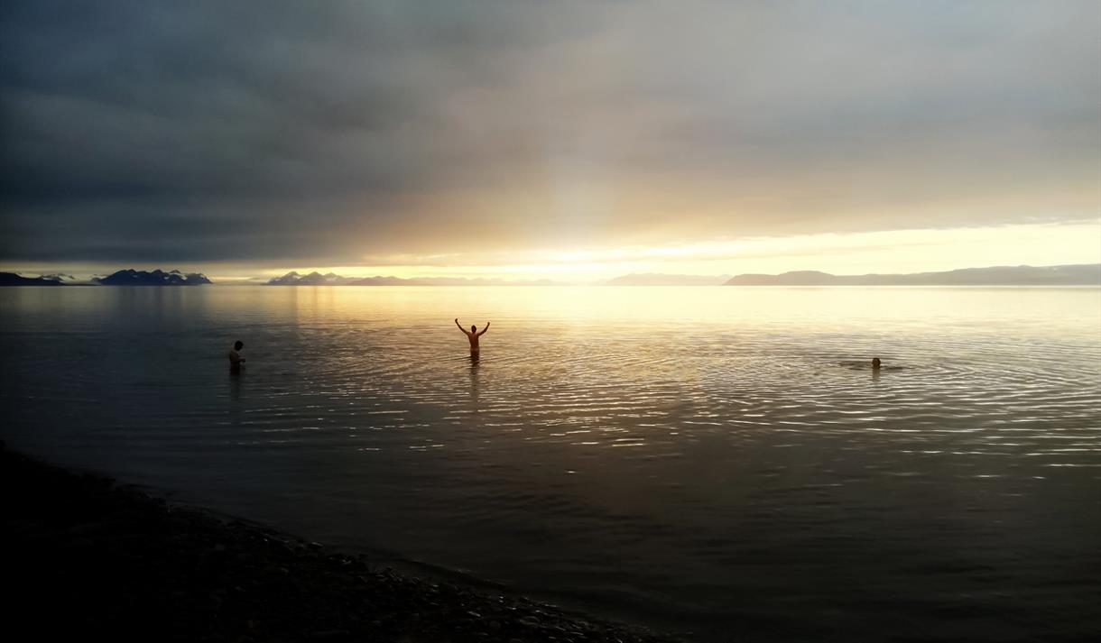 Flere personer som bader på sjøen i solnedgang