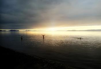 Flere personer som bader på sjøen i solnedgang