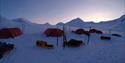 A tent camp with skis lined up around the camp at dusk