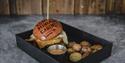 En tallerken med en burger og tilbehør hvor burgerbrødet er svimerket med Coal Miners' Cabins sin logo