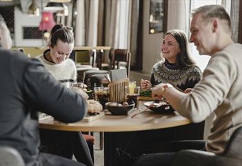 Fire personer sittende rundt et restaurantbord som spiser og prater sammen