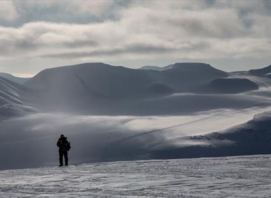 A person standing alone looking out across a snow-covered landscape in the background