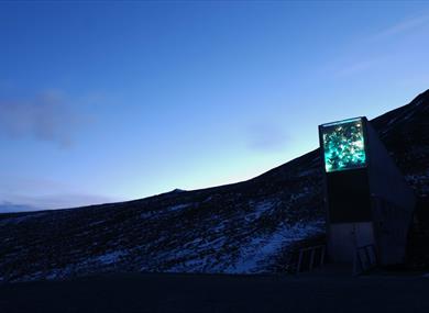 The entrance to Svalbard Global Seed Vault i dark lightly snowy surroundings with a blue and clear evening sky in the background