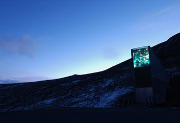 Inngangspartiet til Svalbard Globale Frøhvelv i et mørkt lett snødekt landskap med en klar blå kveldshimmel i bakgrunnen