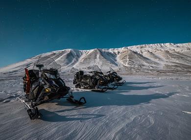 Three snowmobiles out in the wilderness beneath starry skies
