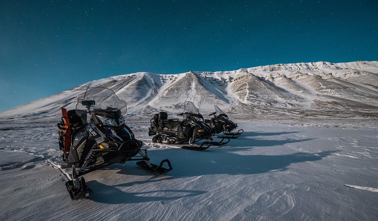Tre snøscootere ute i villmarka under stjernehimmelen