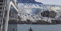 En båt i forgrunnen med en fjord, isbre og et fjell i bakgrunnen
