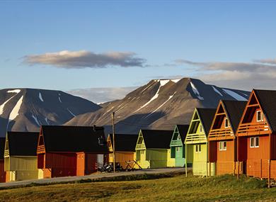 Colourful pointy houses in the foreground with a mountainous landscape and a slightly cloudy blue sky in th ebackground