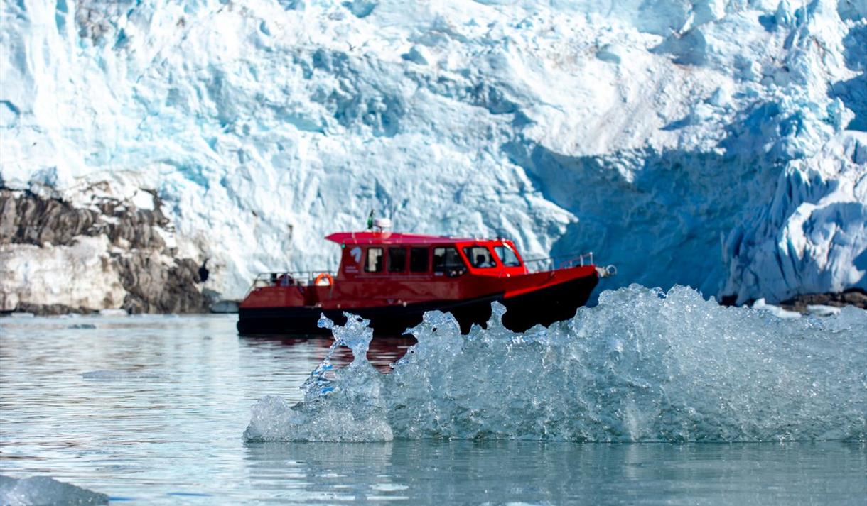 En båt mellom is som flyter i sjøen og en isbre i bakgrunnen