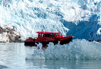 En båt mellom is som flyter i sjøen og en isbre i bakgrunnen