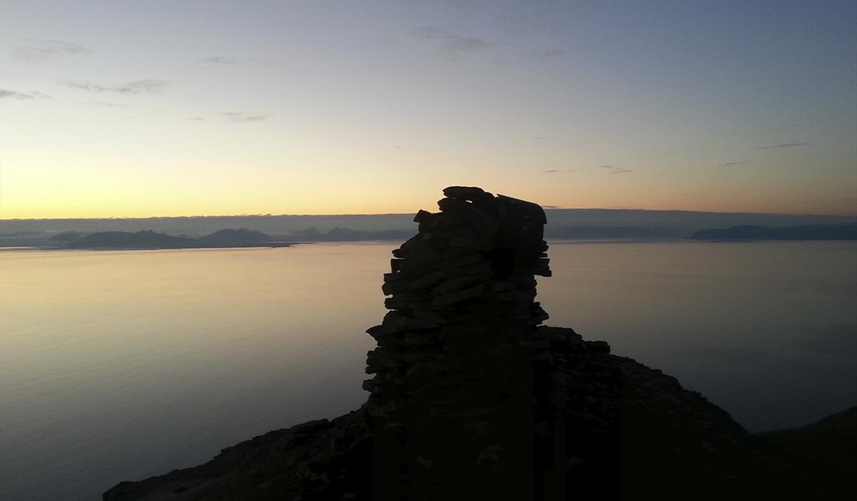 The cairn on top of Fuglefjella in sillhouette against the fjord Isfjorden in dusk light conditions