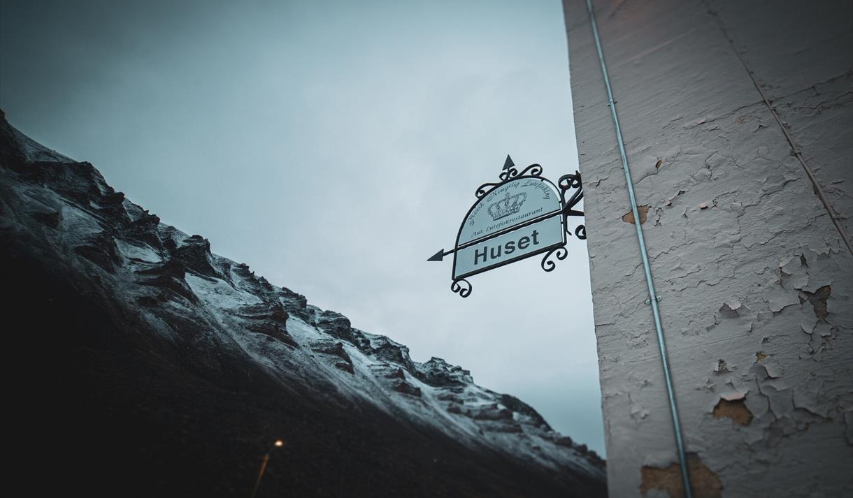 A sign next to the entrance to Huset with mountains in the background