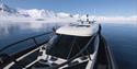 Gjester om bord MS Kvitbjørn i en fjord med rolig blå sjø og snødekte fjell i bakgrunnen