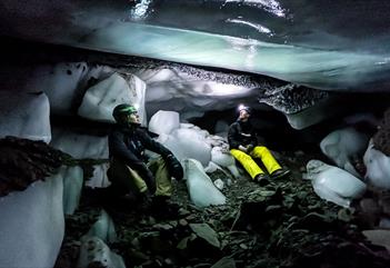 Persons lying inside a dark icecave, lighting up the ice covered cave with a headlamp.