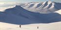 To personer som går opp et fjell på ski med en langstrakt dal og fjellandskap i bakgrunnen