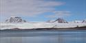 Fjell som stikker opp fra en isbre med en stille fjord i forgrunnen