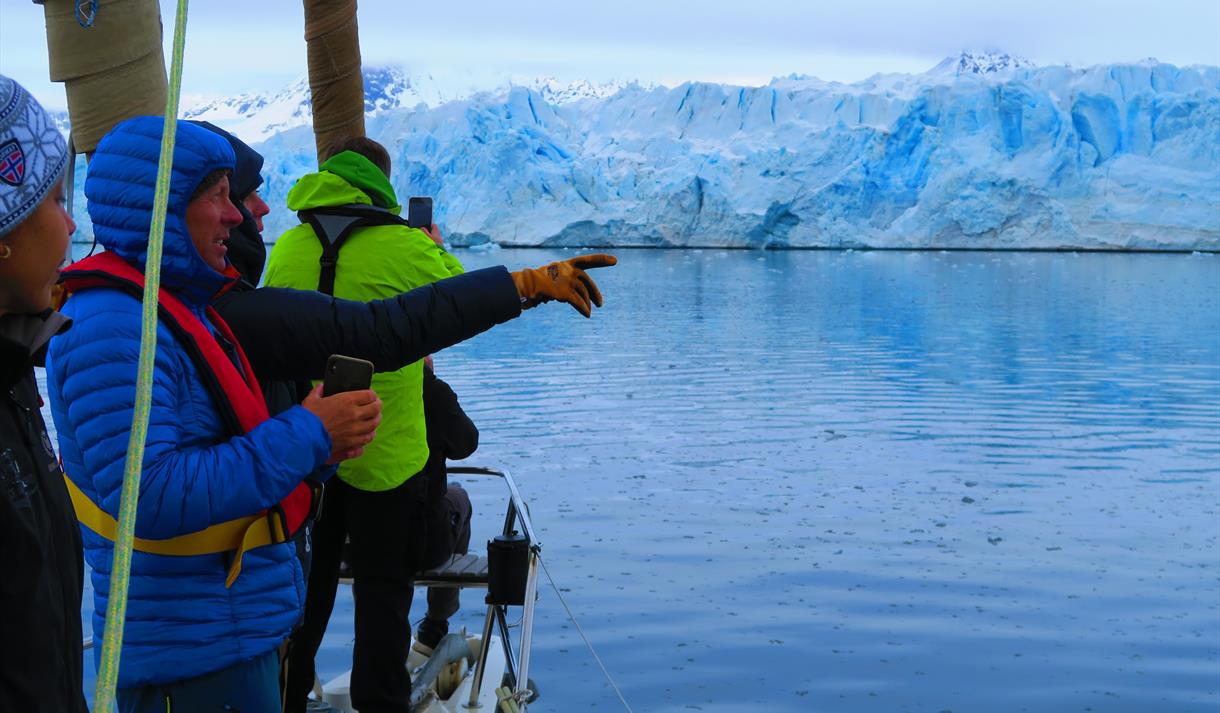 Personer om bord en seilbåt som peker mot en isbre i bakgrunnen