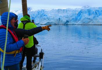 Persons on board a sail boat pointing towards a glacier in the background