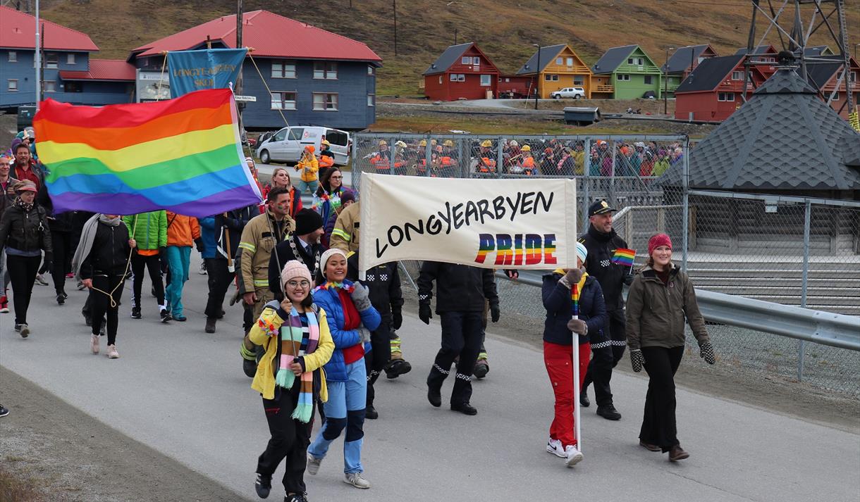 Persons walking in a pride parade for Longyearbyen Pride while carrying a banner and flags