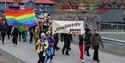 Persons walking in a pride parade for Longyearbyen Pride while carrying a banner and flags