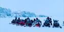Tourgroup with several people and snowmobiles are parked in front of blue glacier ice