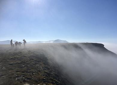 A group of people on top of a mountain with a steep cliff and mist on their right